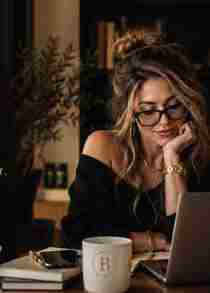 Woman with glasses working beside a laptop and BecomLab mug